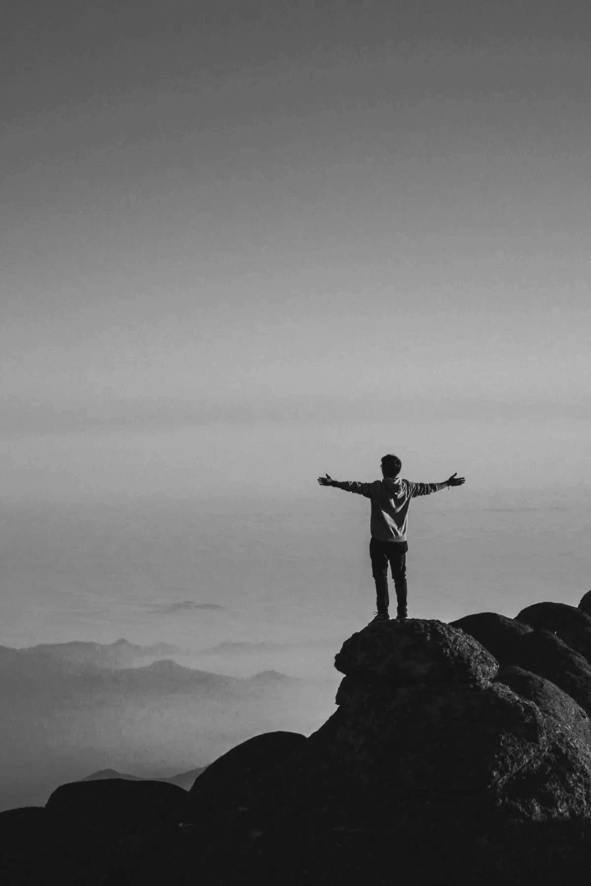 A person standing on a boulder above a sea of clouds, arms spread wide